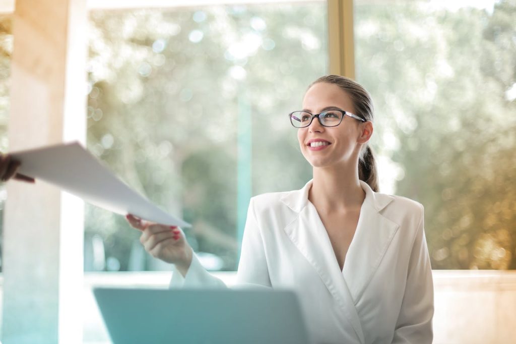 pexels-photo-3756678 Low angle of successful female executive manager in classy style sitting at table with laptop in contemporary workplace and passing documents to colleague